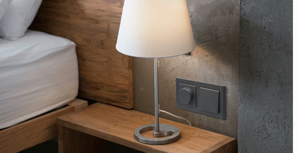 Gniazda i włączniki z serii Ospel Sonata w kolorze szary grafit na tle betonowej ściany w sypialni.